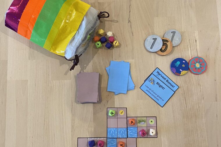 Papas is a tabletop multiplayer game. Pictured are its components, which include a colorful bag of multicolored beads, fake coins, wooden Biodiversity tokens painted with nature scenes, event cards, and farming tiles with farm-related obstructions and spaces for players to place beads.