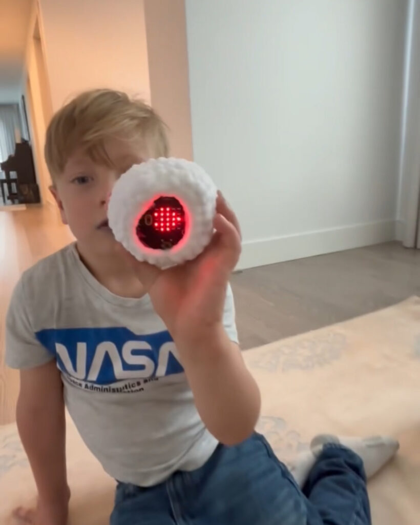 a happy young child holding ZenBitty a plush toy with low tech lLED board showing a red heart that helps him calm down